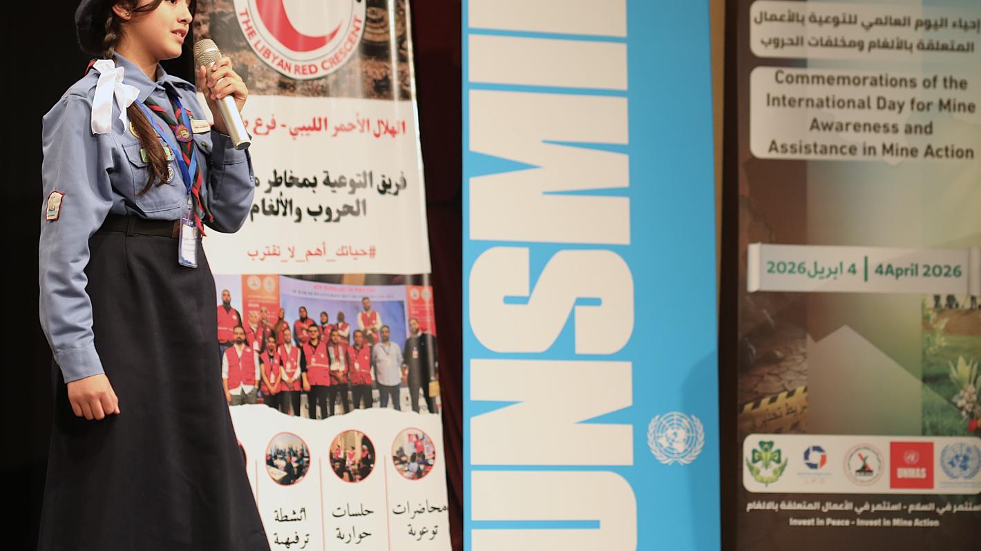 A scout girl holding microphone at the stage with UNSMIL banner