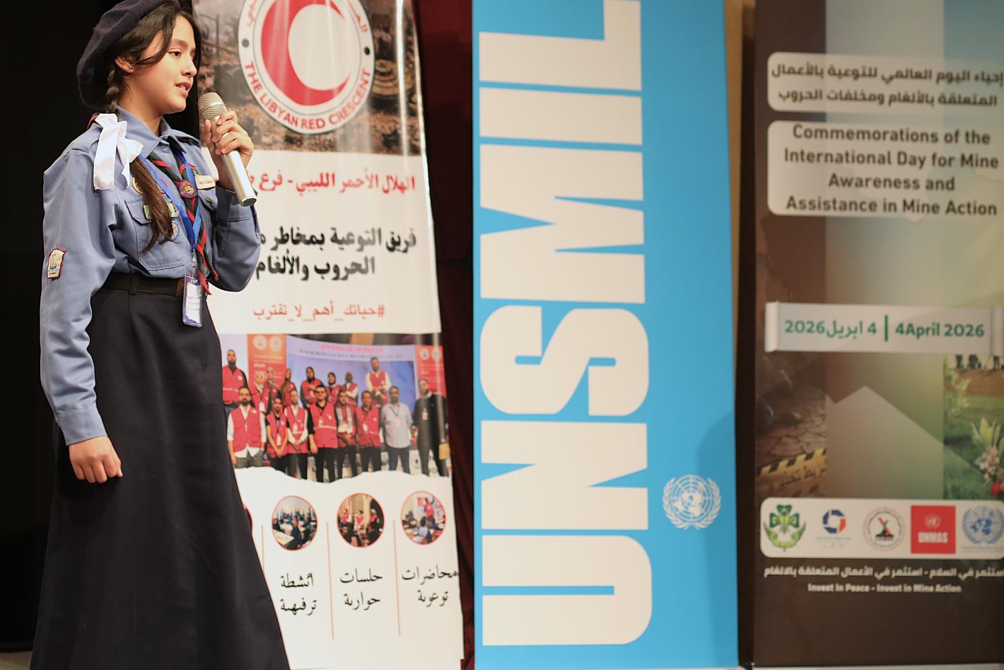 A scout girl holding microphone at the stage with UNSMIL banner